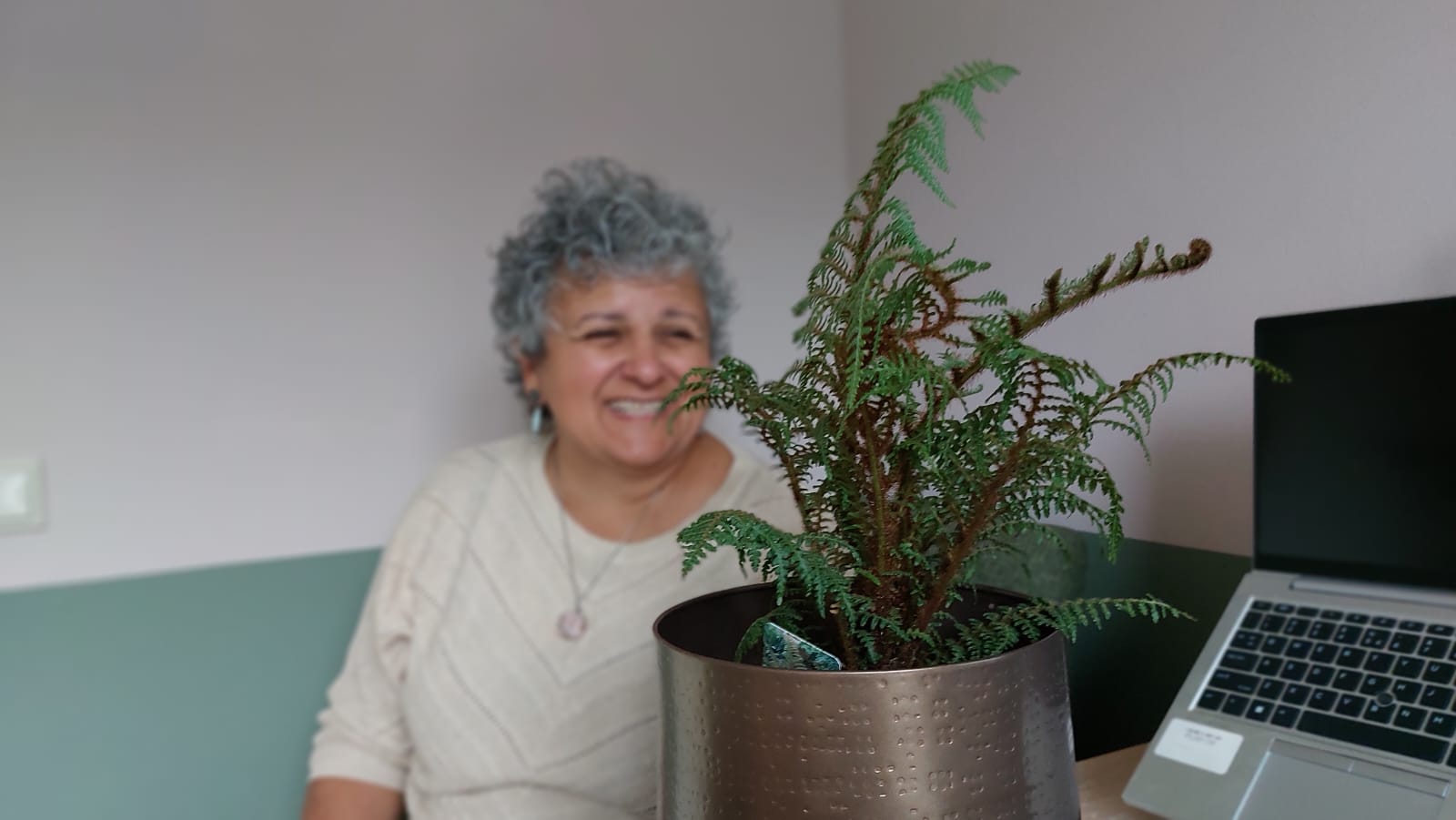 Ivelina glimlacht naast een varen in de praktijkruimte van Koru